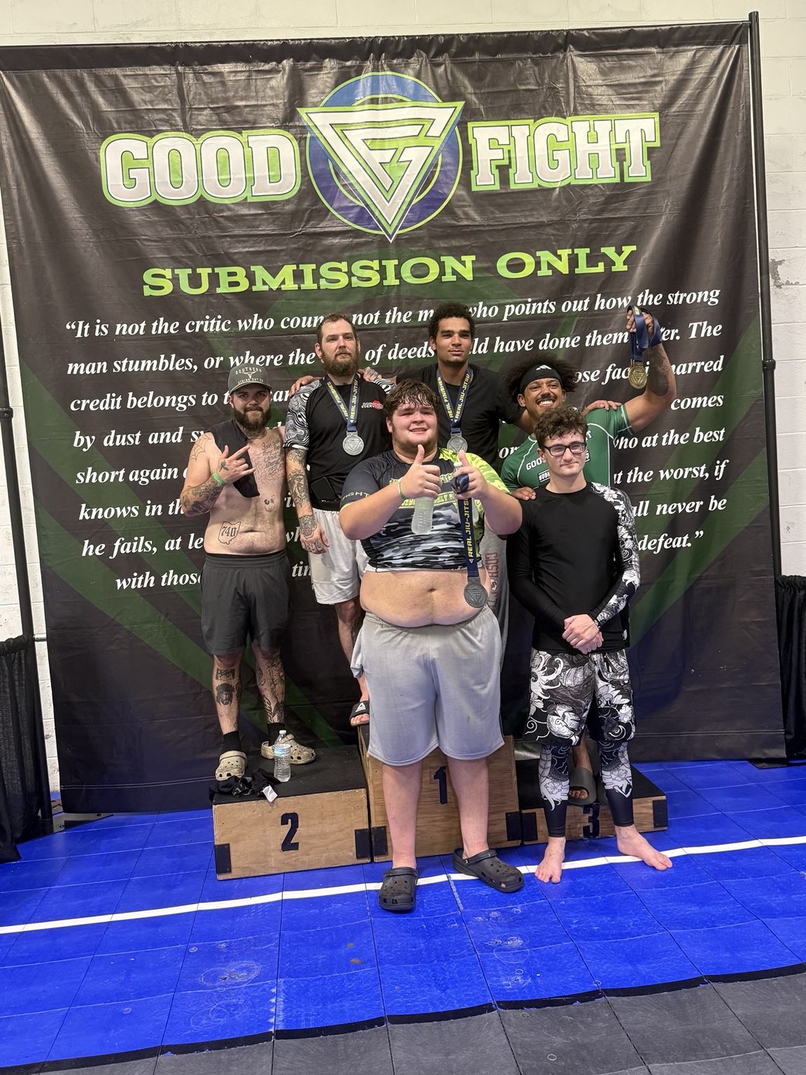 Gym members posing together with medals in front of a Good Fight banner
