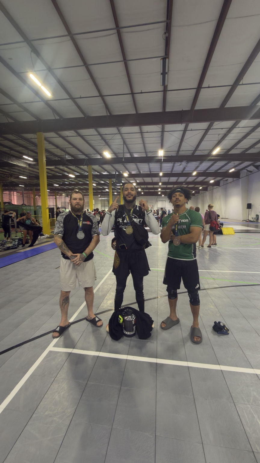 Three gym members wearing medals at a grappling tournament